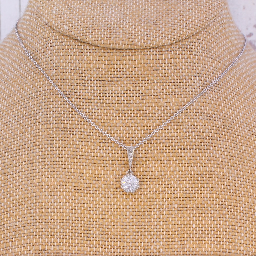 An Art Deco diamond pendant featuring a circular old cut diamond suspended from a linear diamond-set bale on a fine silver-toned chain. View VI