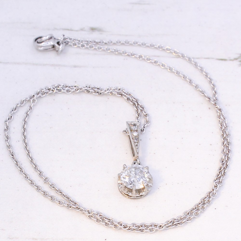An Art Deco diamond pendant featuring a circular old cut diamond suspended from a linear diamond-set bale on a fine silver-toned chain. View VII