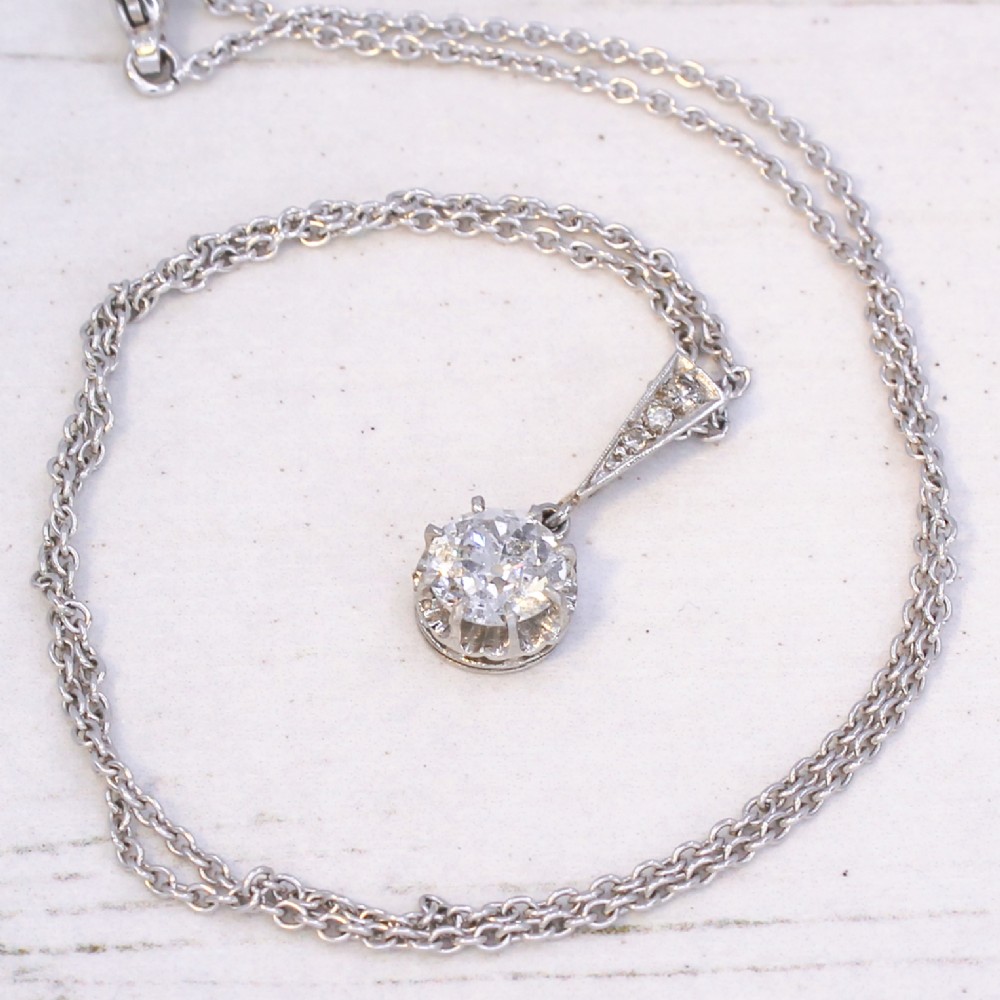 An Art Deco diamond pendant featuring a circular old cut diamond suspended from a linear diamond-set bale on a fine silver-toned chain. View VIII