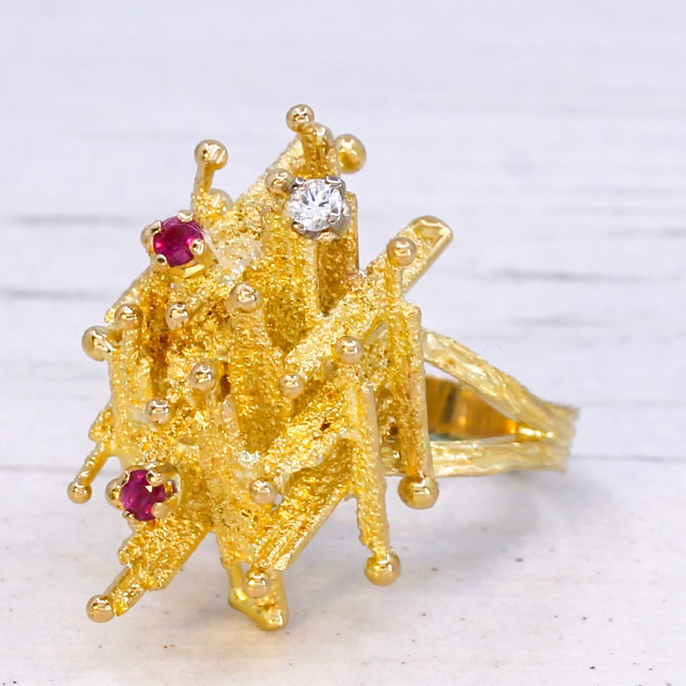 A 1960s textured yellow gold ring featuring an abstract lattice structure set with two round rubies and a single clear diamond.