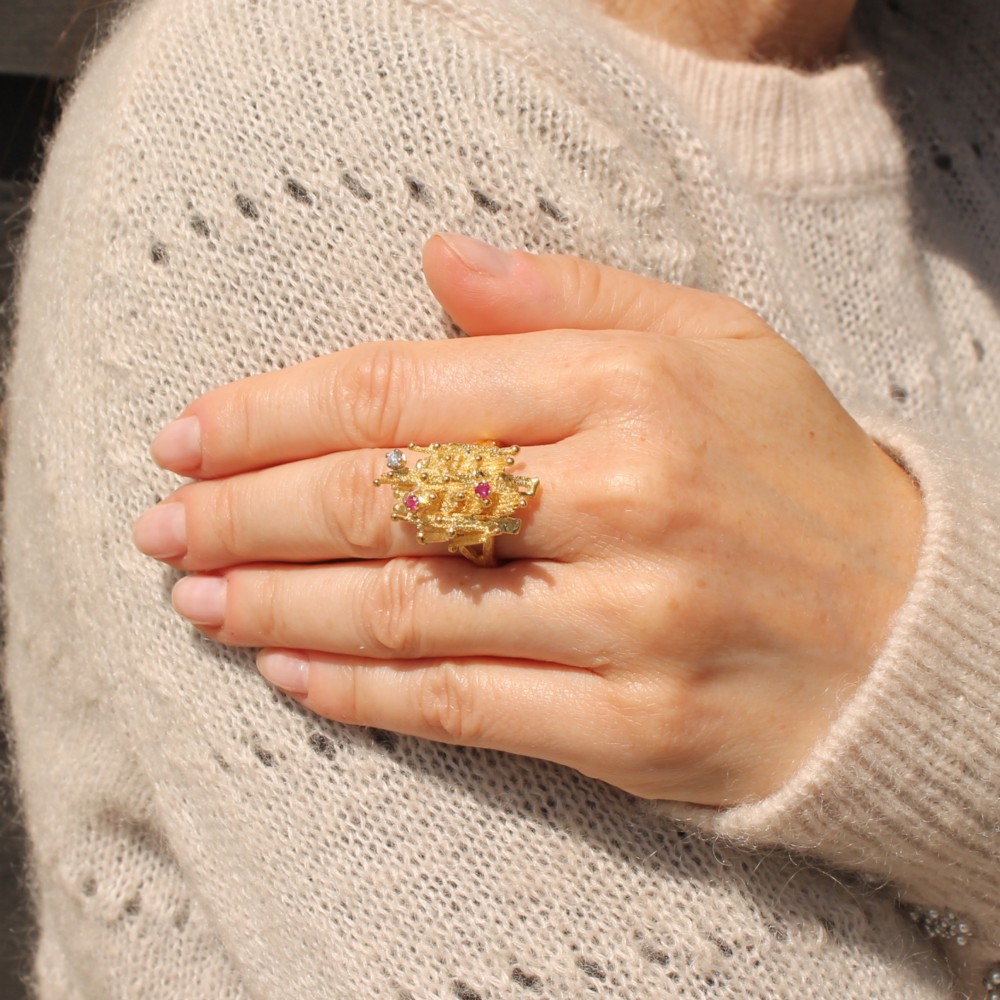 A 1960s textured yellow gold ring featuring an abstract lattice structure set with two round rubies and a single clear diamond. View II
