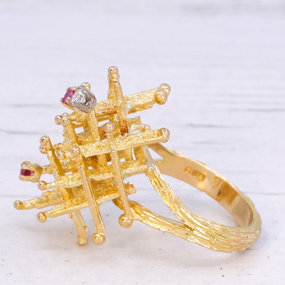 A 1960s textured yellow gold ring featuring an abstract lattice structure set with two round rubies and a single clear diamond. View IV