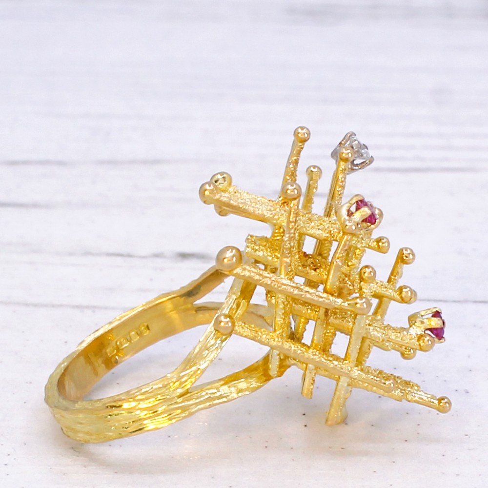 A 1960s textured yellow gold ring featuring an abstract lattice structure set with two round rubies and a single clear diamond. View V