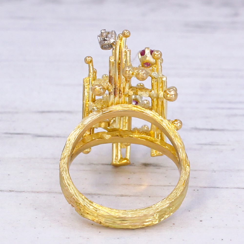 A 1960s textured yellow gold ring featuring an abstract lattice structure set with two round rubies and a single clear diamond. View VI