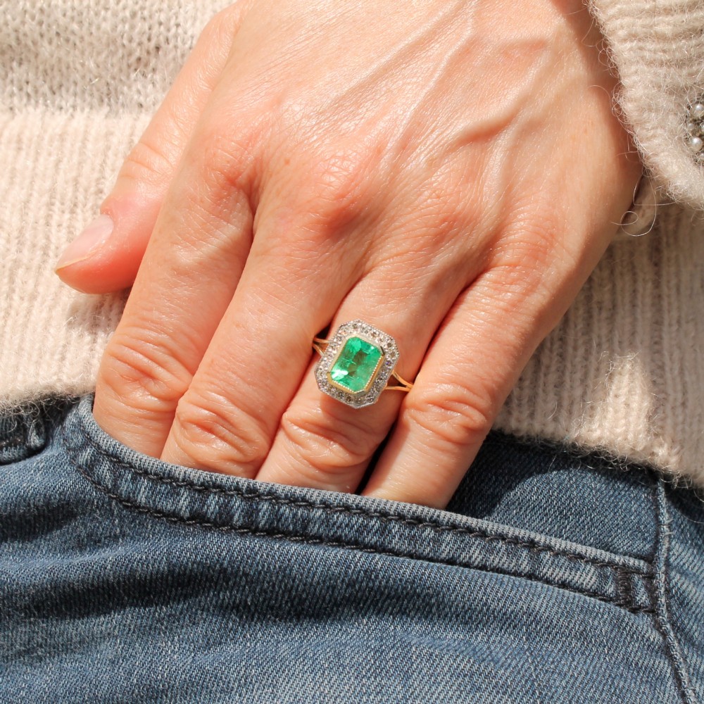 A vintage gold ring featuring a central rectangular green emerald surrounded by a halo of small diamonds. View II
