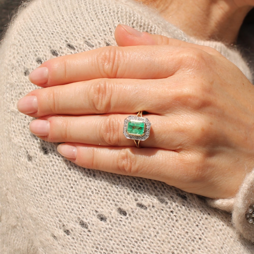 A vintage gold ring featuring a central rectangular green emerald surrounded by a halo of small diamonds. View VI