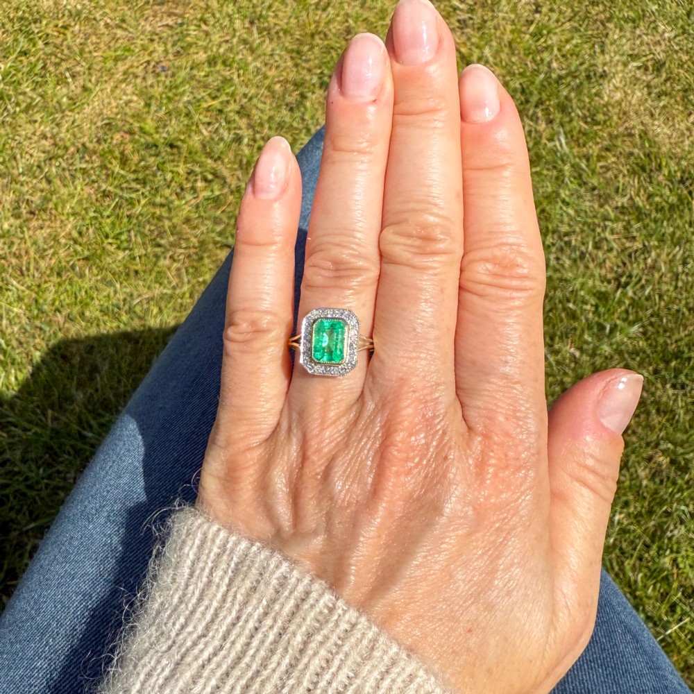 A vintage gold ring featuring a central rectangular green emerald surrounded by a halo of small diamonds. View VII