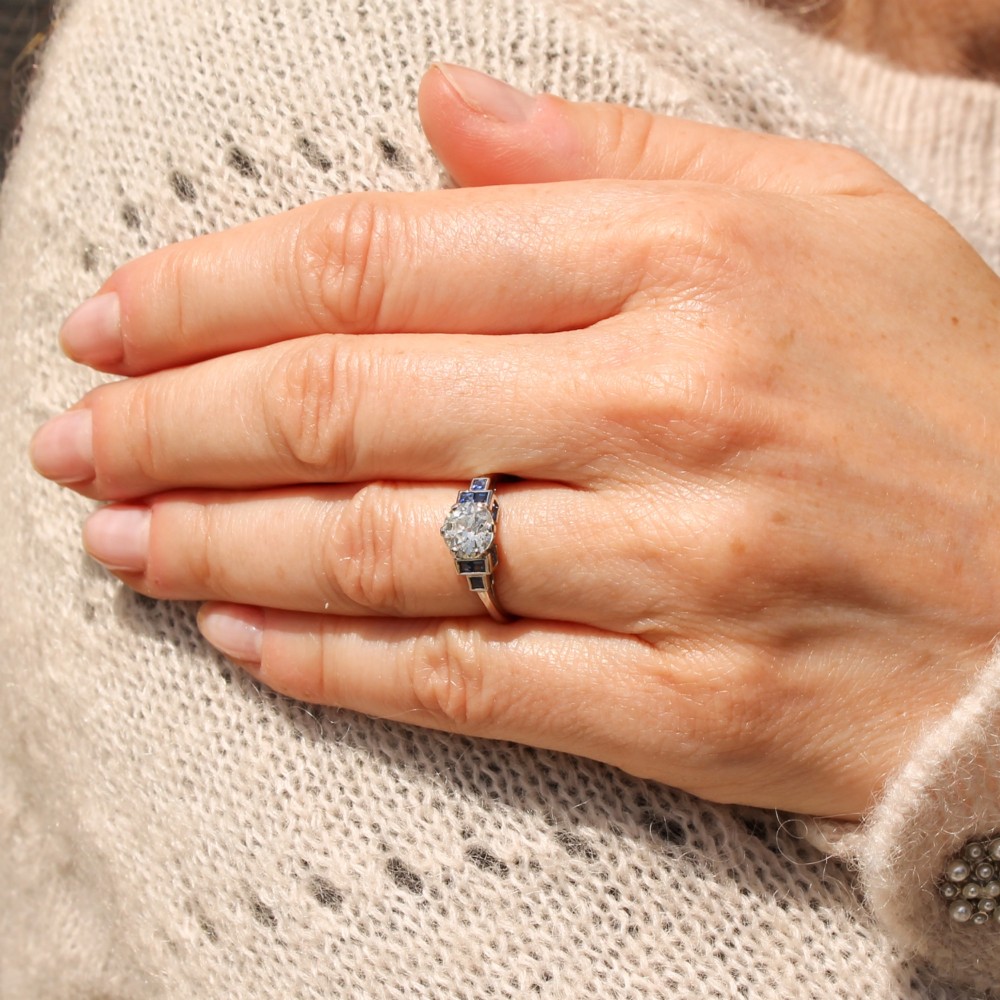 A platinum ring featuring a central round old cut diamond flanked by stepped calibre-cut blue sapphires. View II