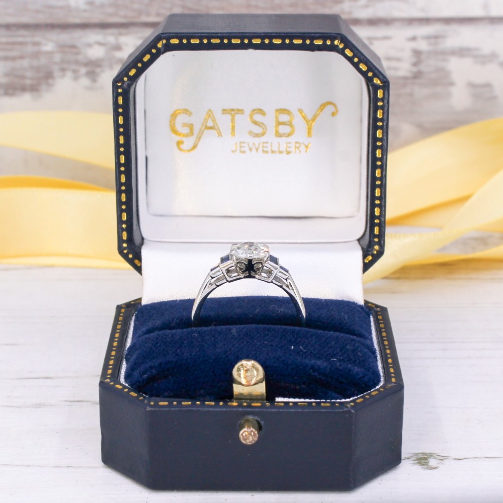A platinum ring featuring a central round old cut diamond flanked by stepped calibre-cut blue sapphires. View IX