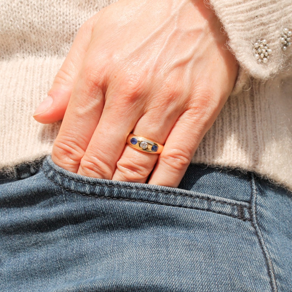 An antique yellow gold gypsy band set with a central old cut diamond flanked by two oval blue sapphires. View II