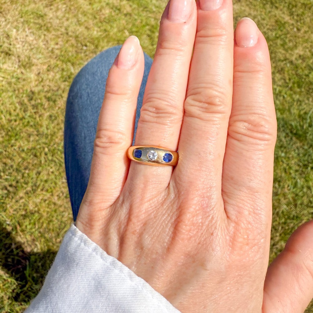 An antique yellow gold gypsy band set with a central old cut diamond flanked by two oval blue sapphires. View VI