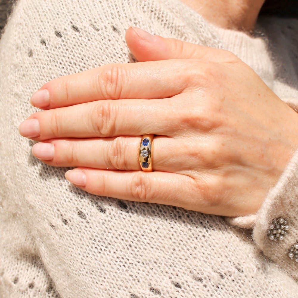 An antique yellow gold gypsy band set with a central old cut diamond flanked by two oval blue sapphires. View VII