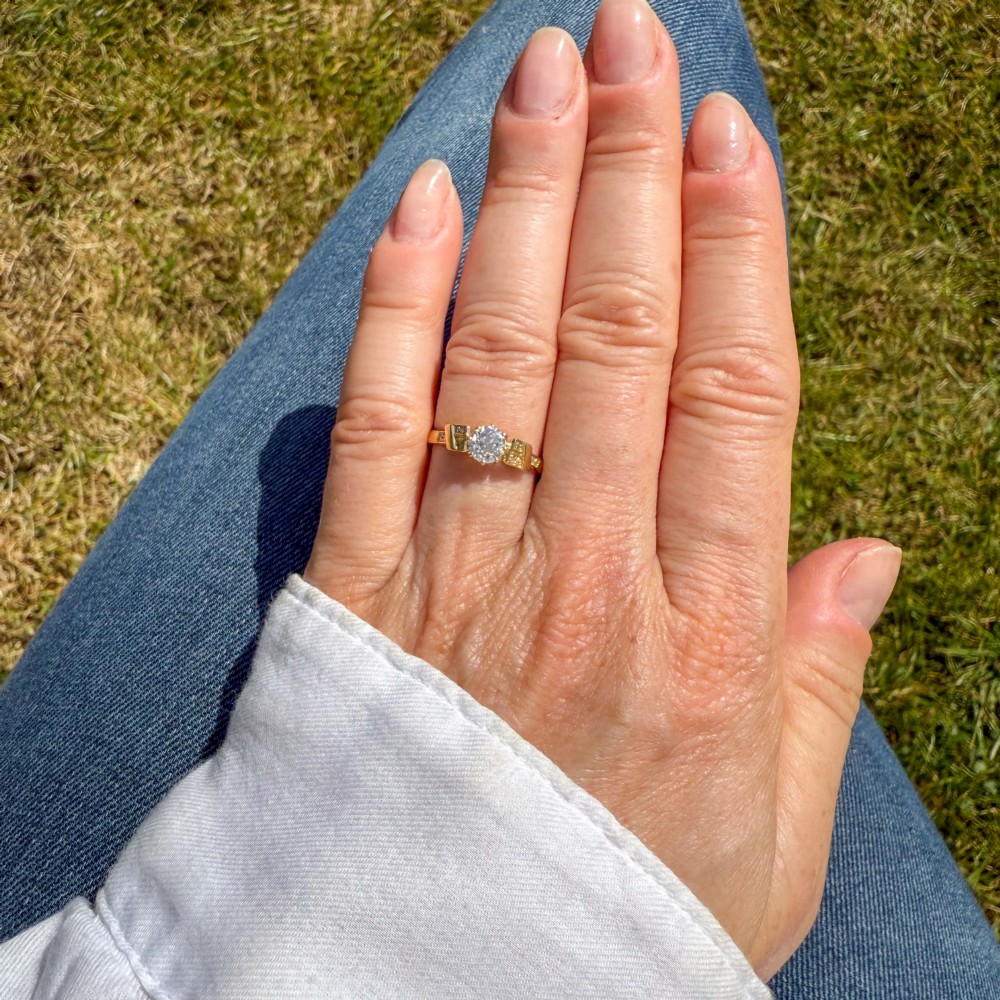 A yellow gold Art Deco engagement ring featuring a central round old cut diamond flanked by geometric stepped shoulders set with small accent diamonds. View VI