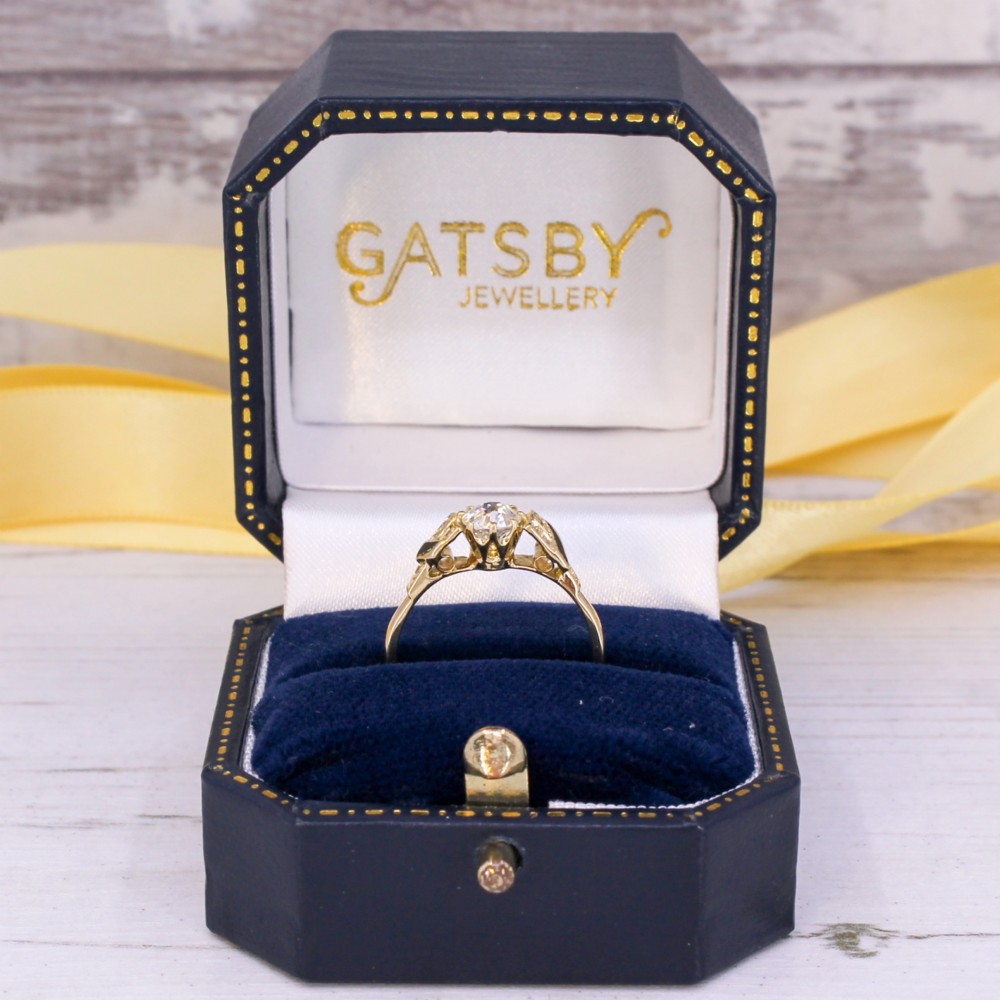 A yellow gold Art Deco engagement ring featuring a central round old cut diamond flanked by geometric stepped shoulders set with small accent diamonds. View IX