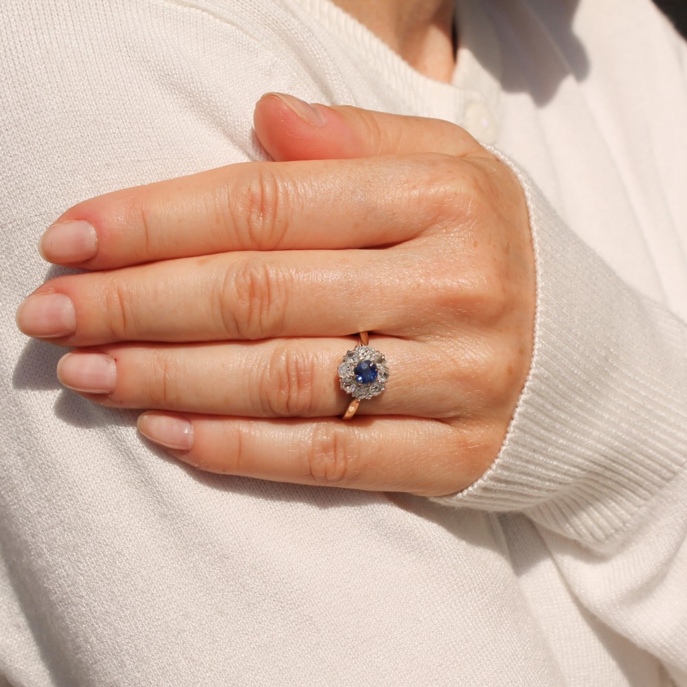 A vintage cluster ring featuring a central round blue sapphire encircled by nine brilliant-cut diamonds set on a yellow gold band. View VI