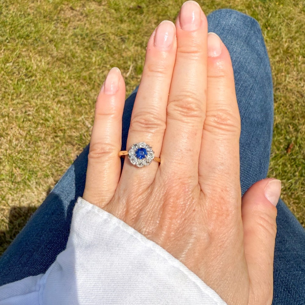 A vintage cluster ring featuring a central round blue sapphire encircled by nine brilliant-cut diamonds set on a yellow gold band. View VII