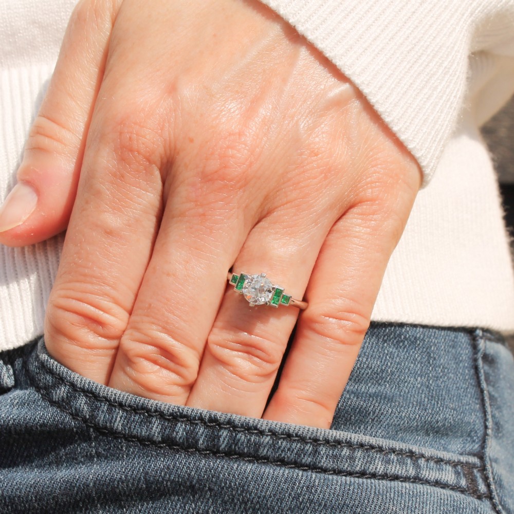 A platinum ring set with a central round old European cut diamond flanked by channel-set green emerald shoulders. View II
