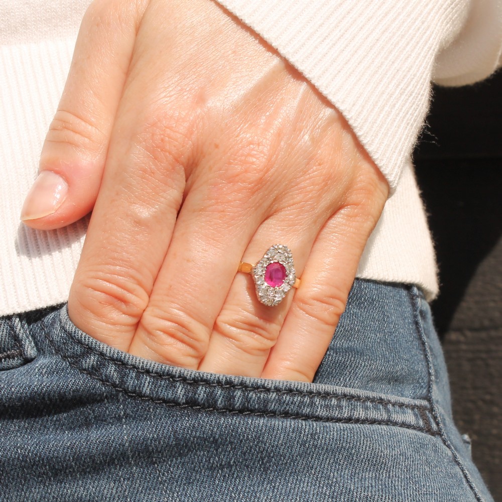 A Victorian ruby and diamond cluster ring featuring an oval red central ruby encased by old-cut diamonds on a yellow gold band. View II