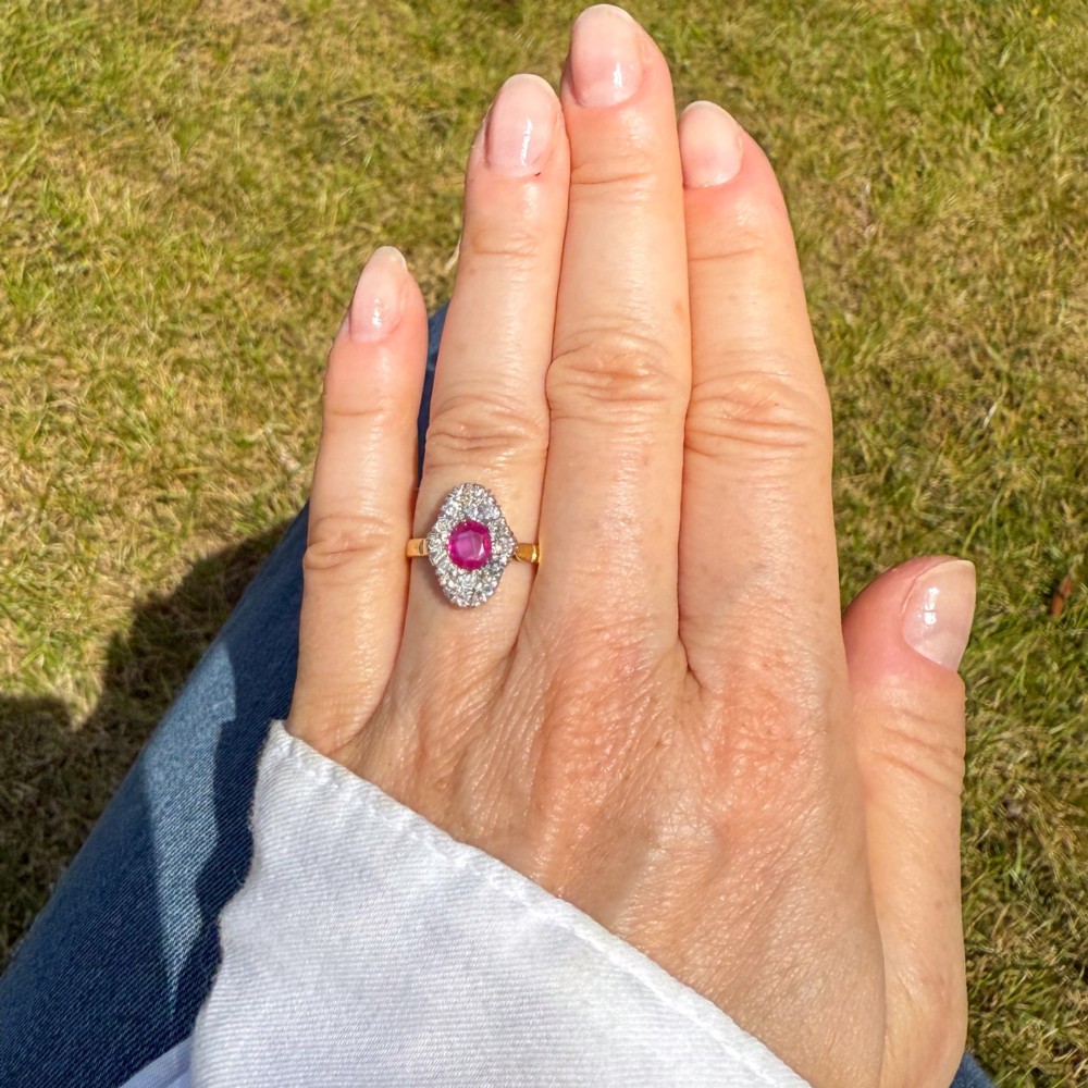 A Victorian ruby and diamond cluster ring featuring an oval red central ruby encased by old-cut diamonds on a yellow gold band. View VI