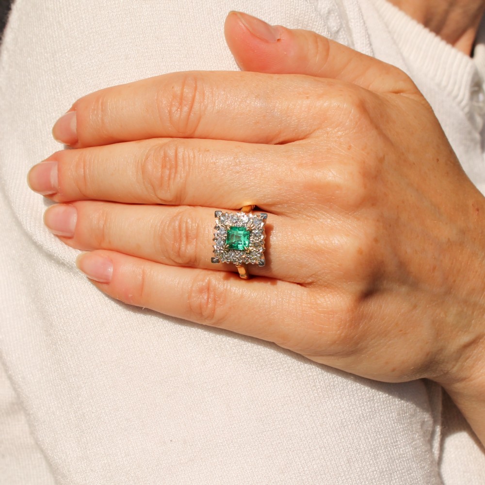 A vintage 1950s dress ring featuring a square green emerald framed by a square halo of diamonds set in a yellow gold band. View II