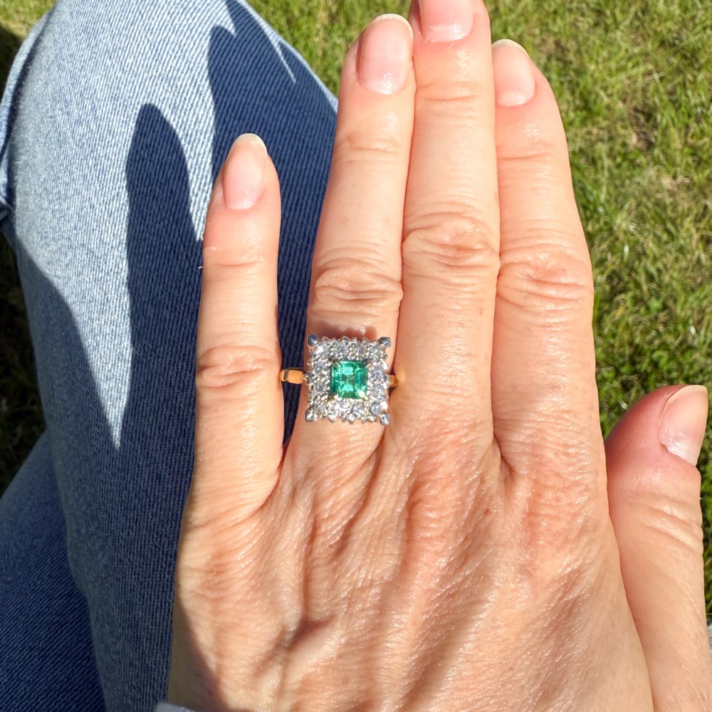A vintage 1950s dress ring featuring a square green emerald framed by a square halo of diamonds set in a yellow gold band. View VI