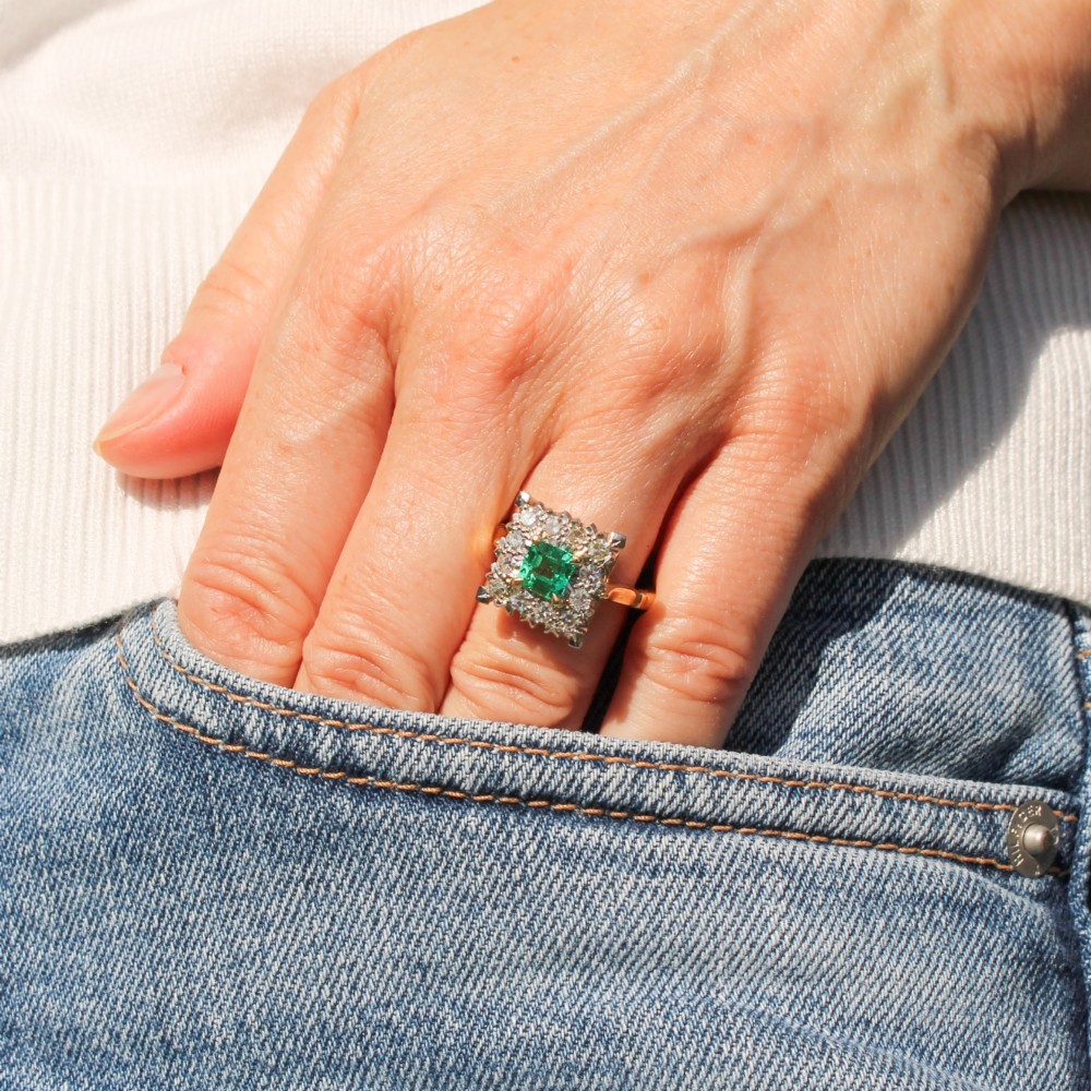 A vintage 1950s dress ring featuring a square green emerald framed by a square halo of diamonds set in a yellow gold band. View VII