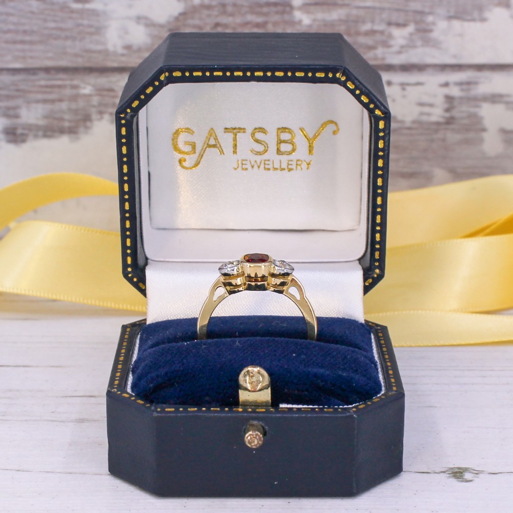 A yellow gold three-stone ring featuring a central cushion cut red ruby set in a bezel, flanked by two old-cut round diamonds. View IX