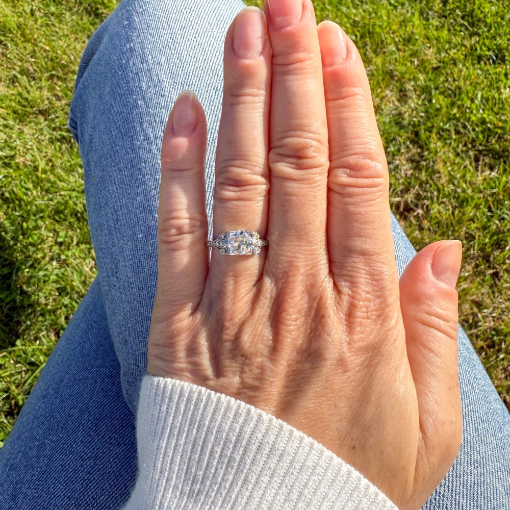An Edwardian platinum ring featuring a central old cut diamond within pierced filigree shoulders and an engraved band. View VI
