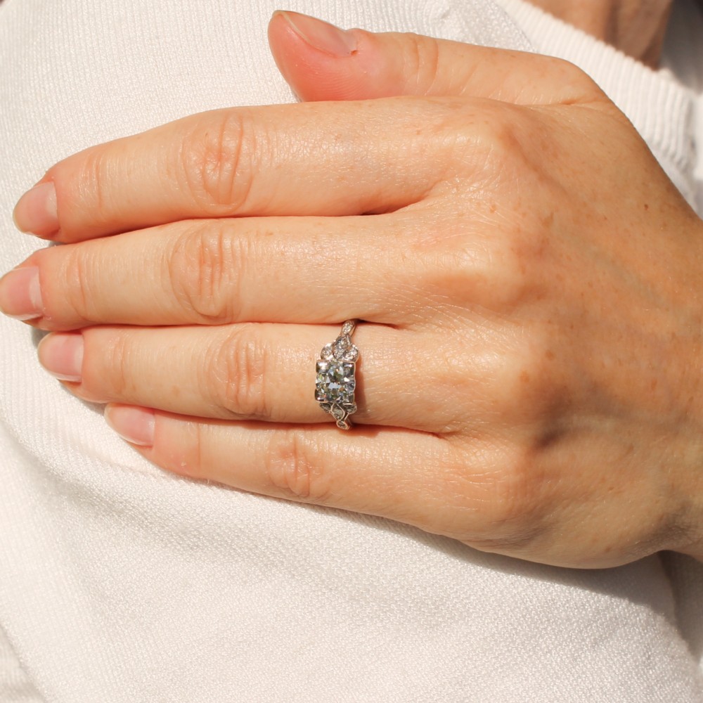 An Edwardian platinum ring featuring a central old cut diamond within pierced filigree shoulders and an engraved band. View VII