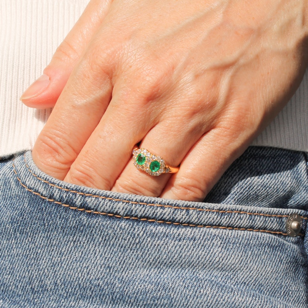 A late Victorian yellow gold double cluster ring set with two bright green oval emeralds, each surrounded by a halo of old-cut diamonds. View II