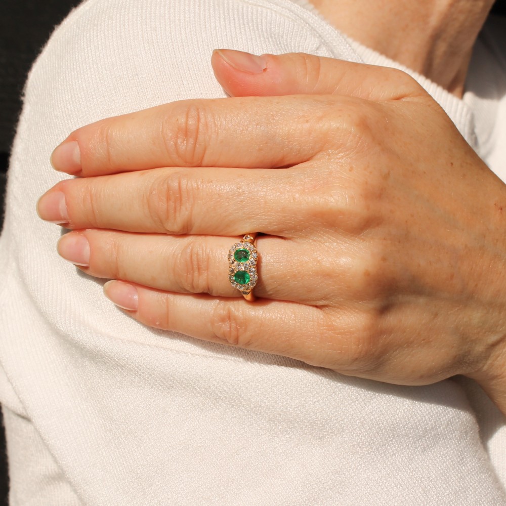 A late Victorian yellow gold double cluster ring set with two bright green oval emeralds, each surrounded by a halo of old-cut diamonds. View VI