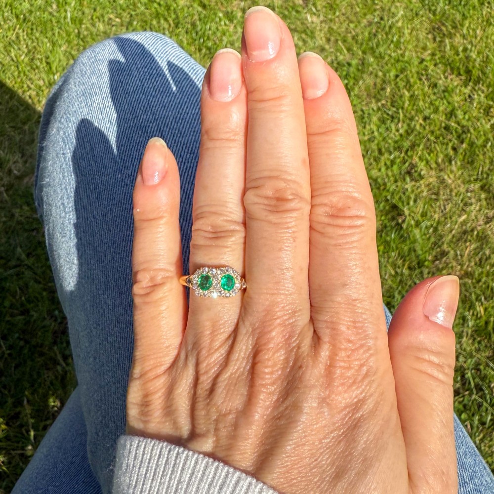 A late Victorian yellow gold double cluster ring set with two bright green oval emeralds, each surrounded by a halo of old-cut diamonds. View VII