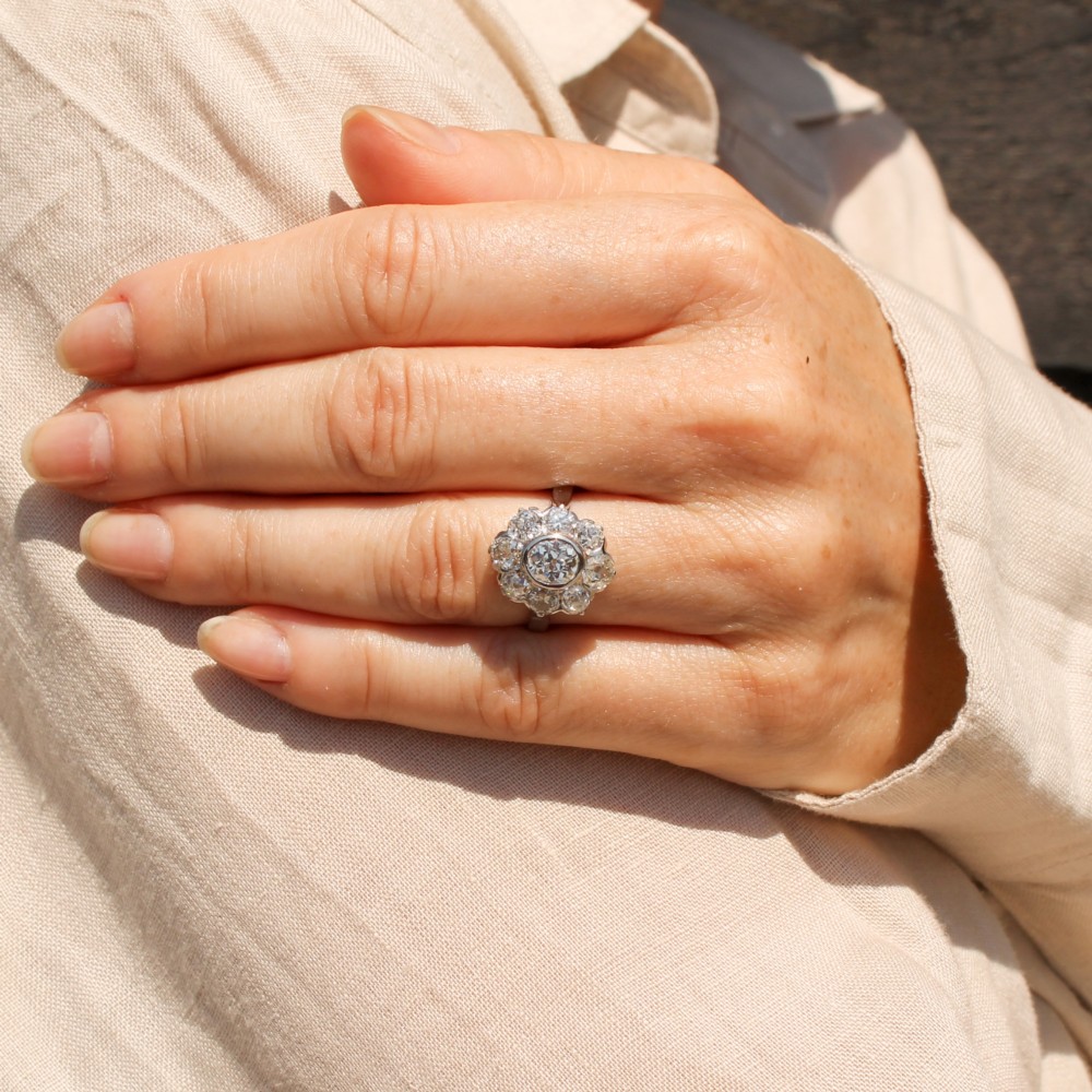 A vintage platinum ring featuring a central old cut diamond surrounded by a halo of eight smaller diamonds in a floral cluster setting on a smooth band. View II