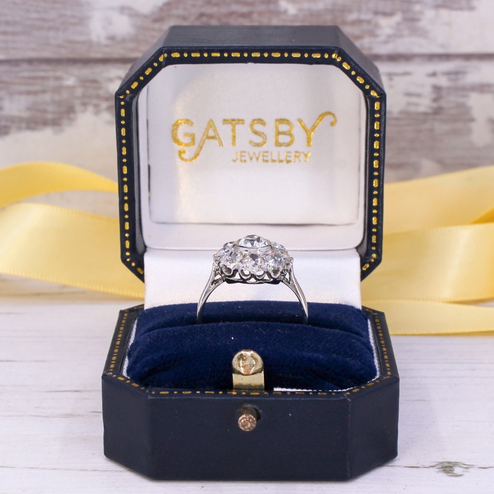A vintage platinum ring featuring a central old cut diamond surrounded by a halo of eight smaller diamonds in a floral cluster setting on a smooth band. View IX