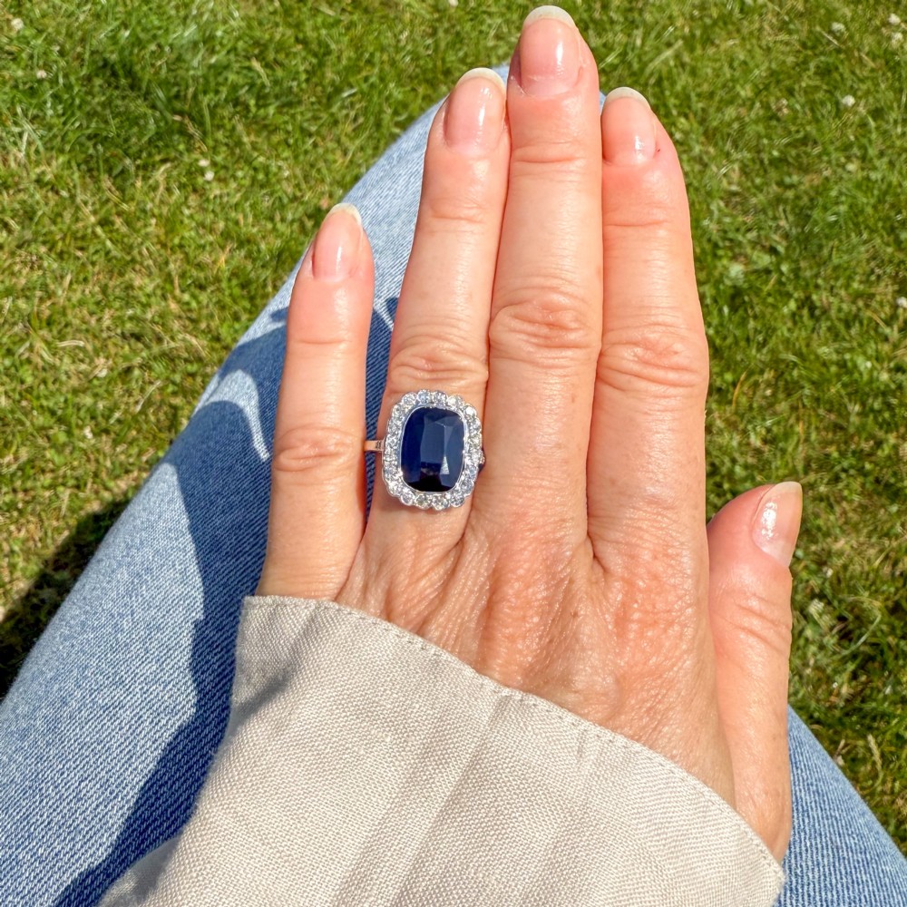 A vintage platinum ring featuring a cushion-cut dark blue sapphire encircled by a halo of brilliant-cut diamonds. View II