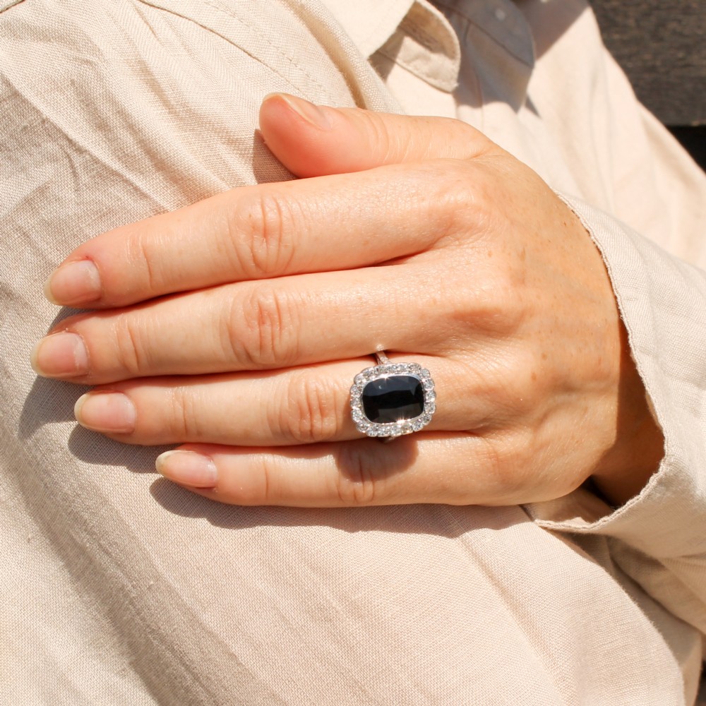 A vintage platinum ring featuring a cushion-cut dark blue sapphire encircled by a halo of brilliant-cut diamonds. View VI