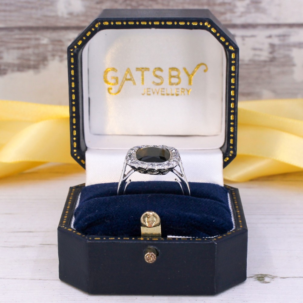 A vintage platinum ring featuring a cushion-cut dark blue sapphire encircled by a halo of brilliant-cut diamonds. View IX