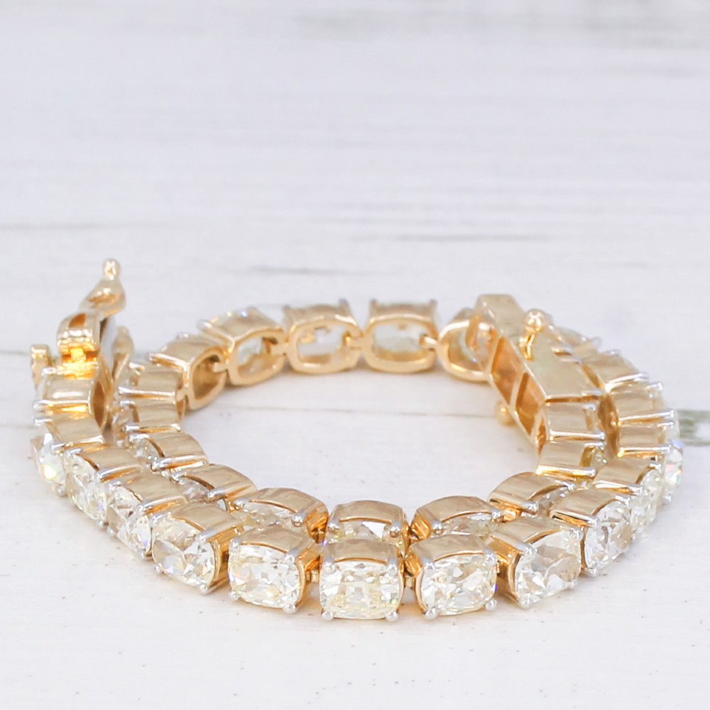 A yellow gold tennis bracelet set with a continuous row of cushion-shaped old mine cut diamonds featuring claw mounts and a box clasp. View IV