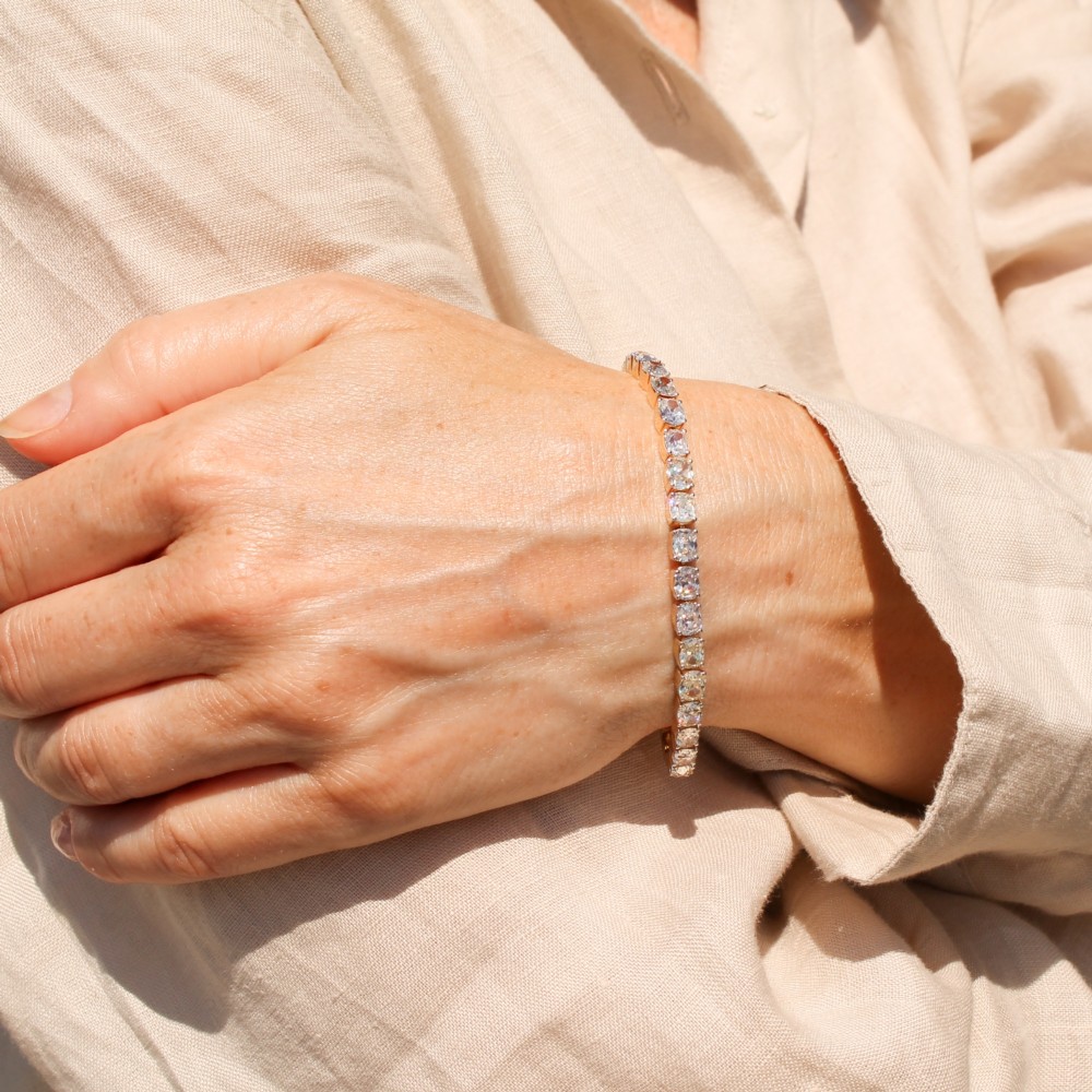 A yellow gold tennis bracelet set with a continuous row of cushion-shaped old mine cut diamonds featuring claw mounts and a box clasp. View V
