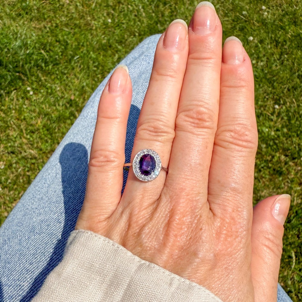 An Art Deco ring featuring an oval deep blue sapphire surrounded by a halo of small diamonds set on a slender silver tone band. View II