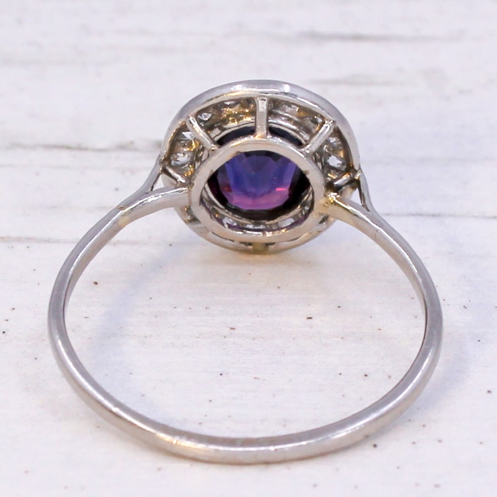 An Art Deco ring featuring an oval deep blue sapphire surrounded by a halo of small diamonds set on a slender silver tone band. View V