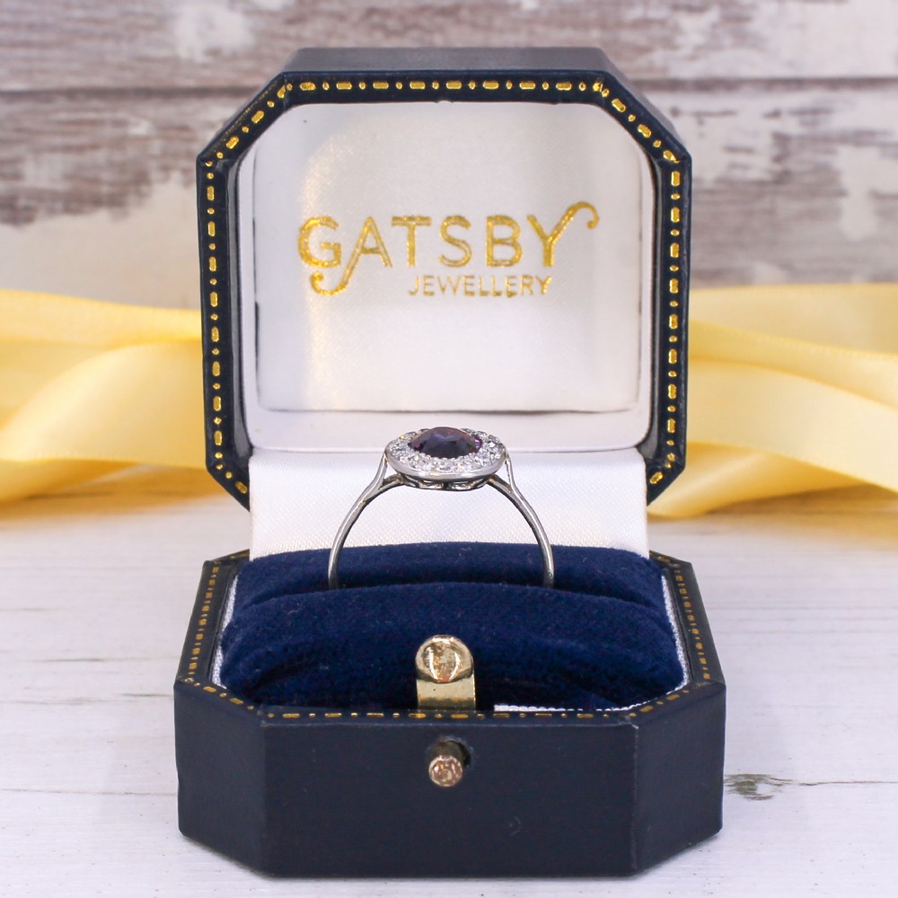 An Art Deco ring featuring an oval deep blue sapphire surrounded by a halo of small diamonds set on a slender silver tone band. View IX