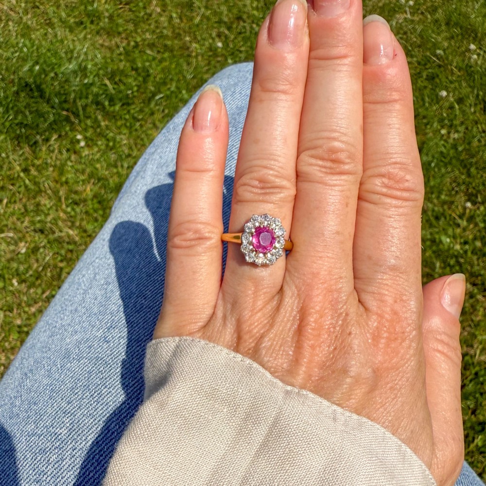 An antique gold ring featuring a central oval pink sapphire set in gold claws, surrounded by a halo of brilliant old-cut diamonds set on a smooth yellow gold band. View VI