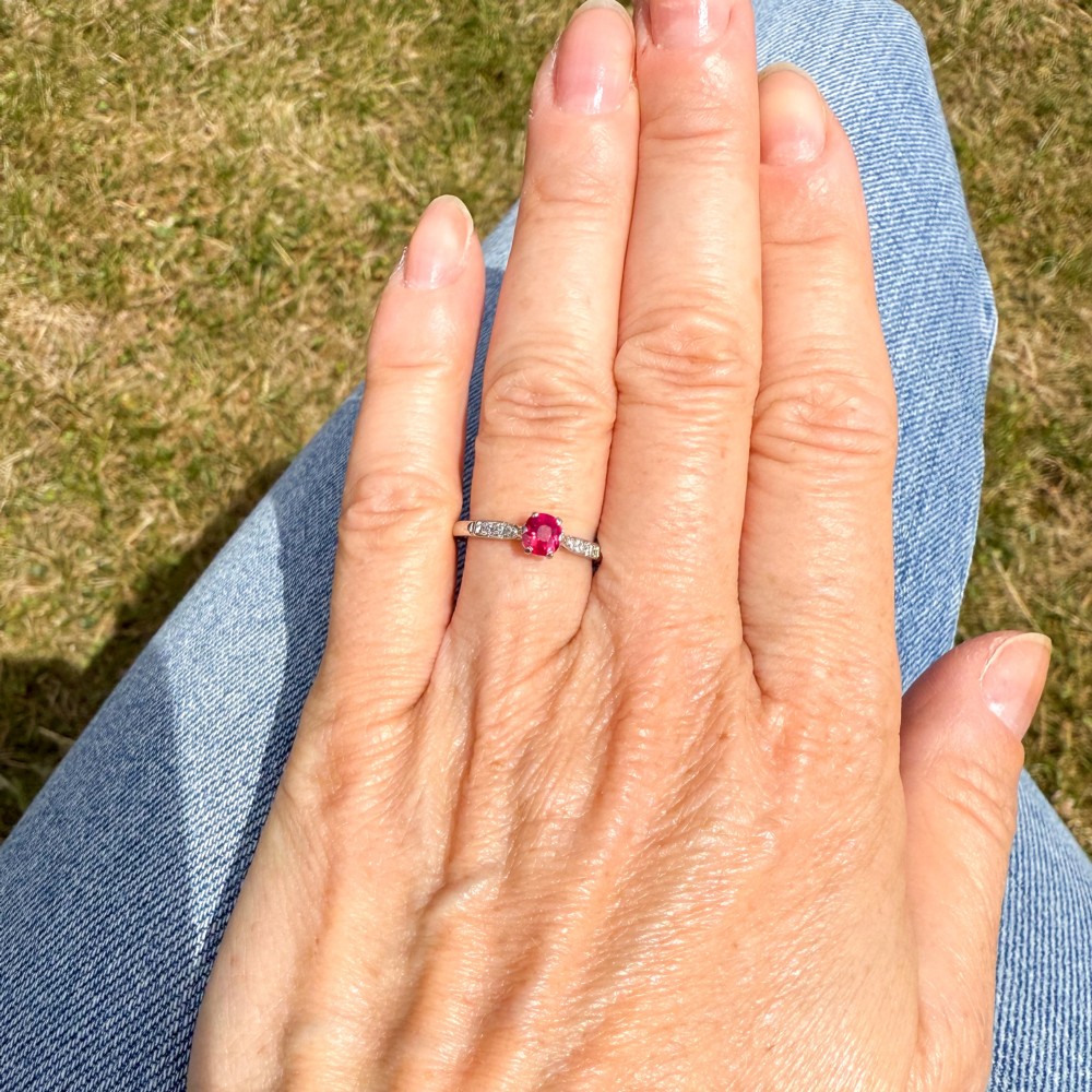 A vintage platinum ring featuring a central round red ruby flanked by diamond-set shoulders. View VI