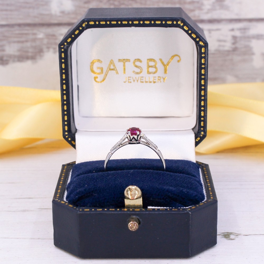 A vintage platinum ring featuring a central round red ruby flanked by diamond-set shoulders. View IX
