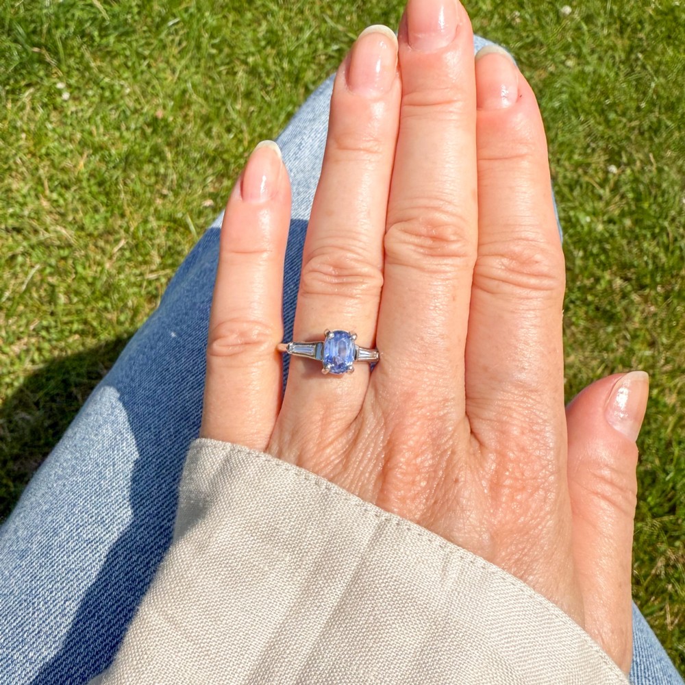 A vintage platinum ring featuring a central oval light blue sapphire flanked by two tapered baguette diamonds. View II