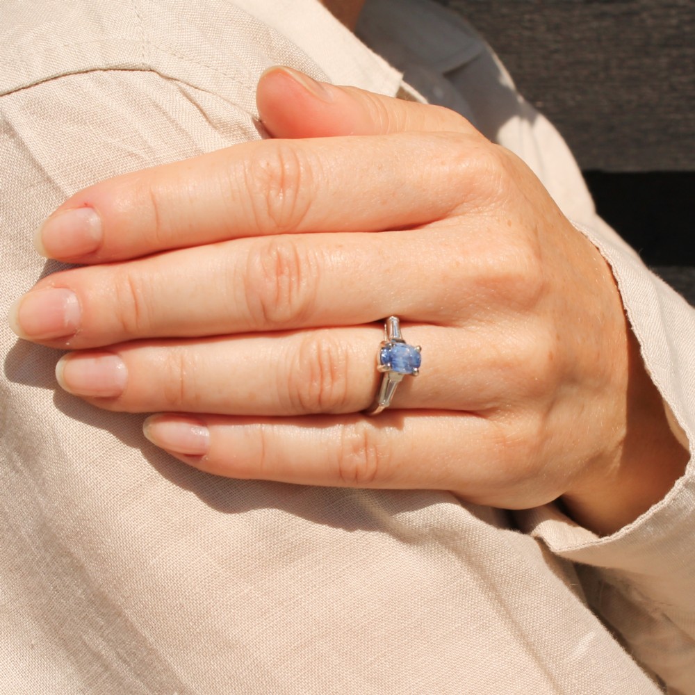 A vintage platinum ring featuring a central oval light blue sapphire flanked by two tapered baguette diamonds. View VII