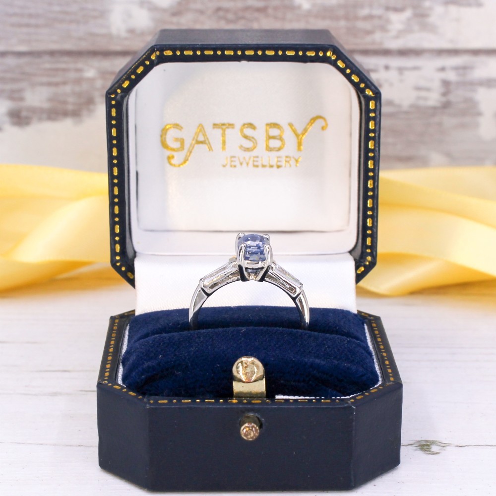 A vintage platinum ring featuring a central oval light blue sapphire flanked by two tapered baguette diamonds. View IX