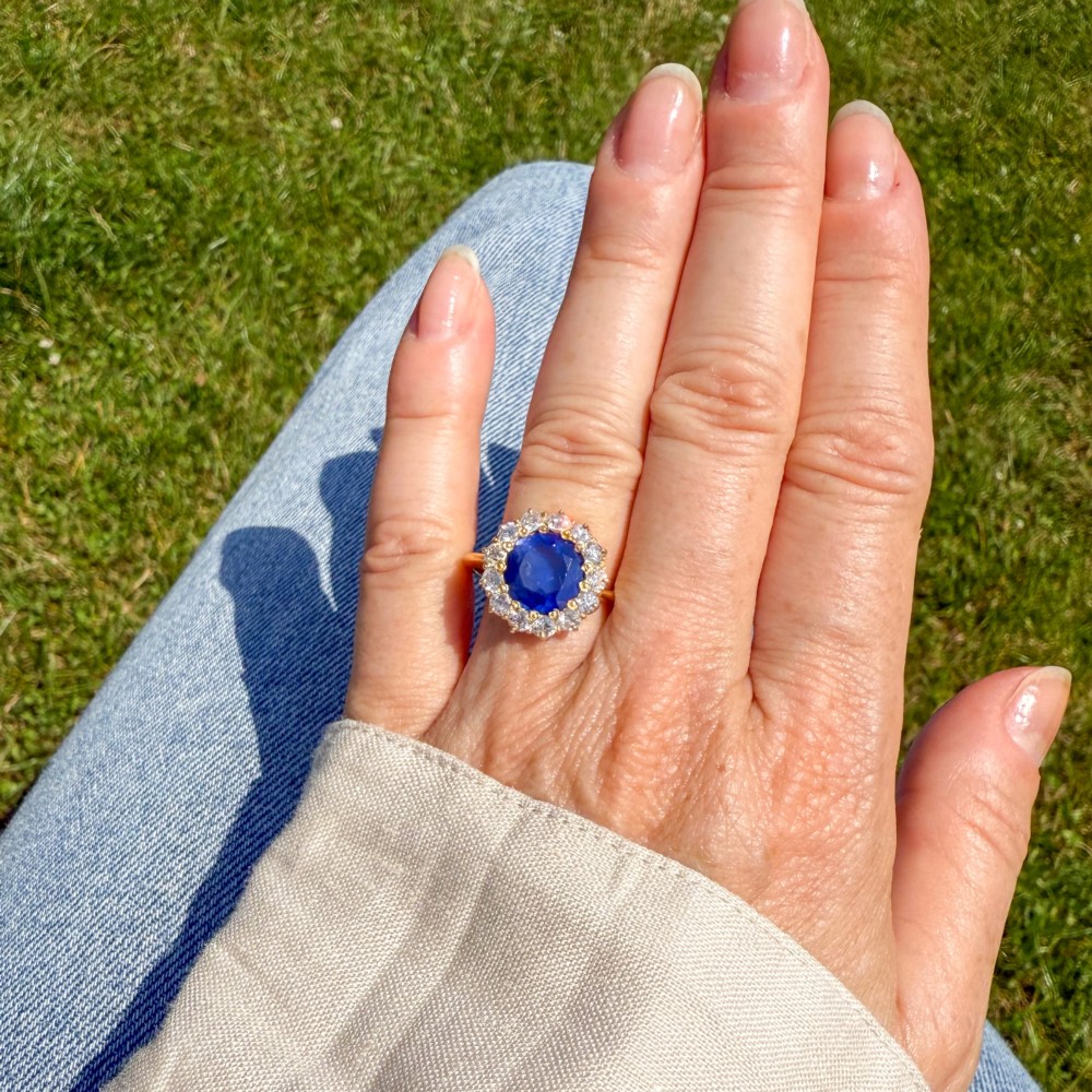 An Edwardian cluster ring set with a circular blue central sapphire framed by a halo of old cut diamonds on a yellow gold band. View VI