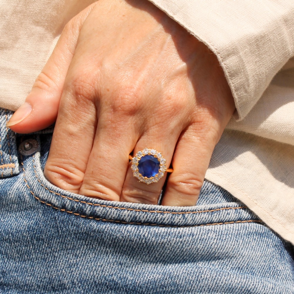 An Edwardian cluster ring set with a circular blue central sapphire framed by a halo of old cut diamonds on a yellow gold band. View VII